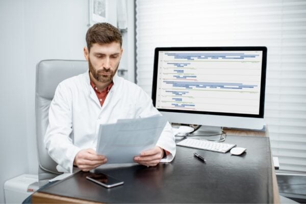 A doctor is reviewing paperwork at a desk in his office